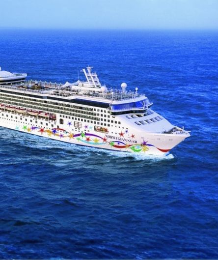 Das große weiße Kreuzfahrtschiff „Norwegian Star“ mit bunt bemaltem Rumpf fährt auf dem tiefblauen, leicht welligen Meer. Das große weiße Kreuzfahrtschiff „Norwegian Star“ mit bunt bemaltem Rumpf fährt auf dem tiefblauen, leicht welligen Meer.